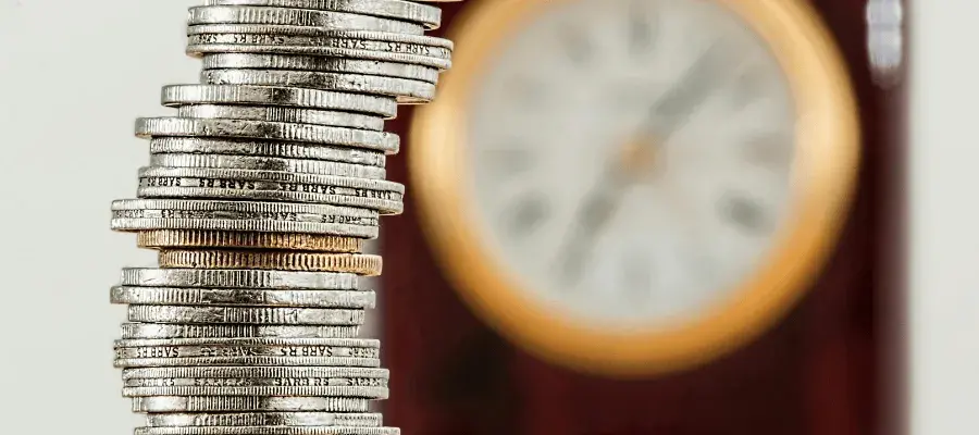 stacked coins with blurred clock in background