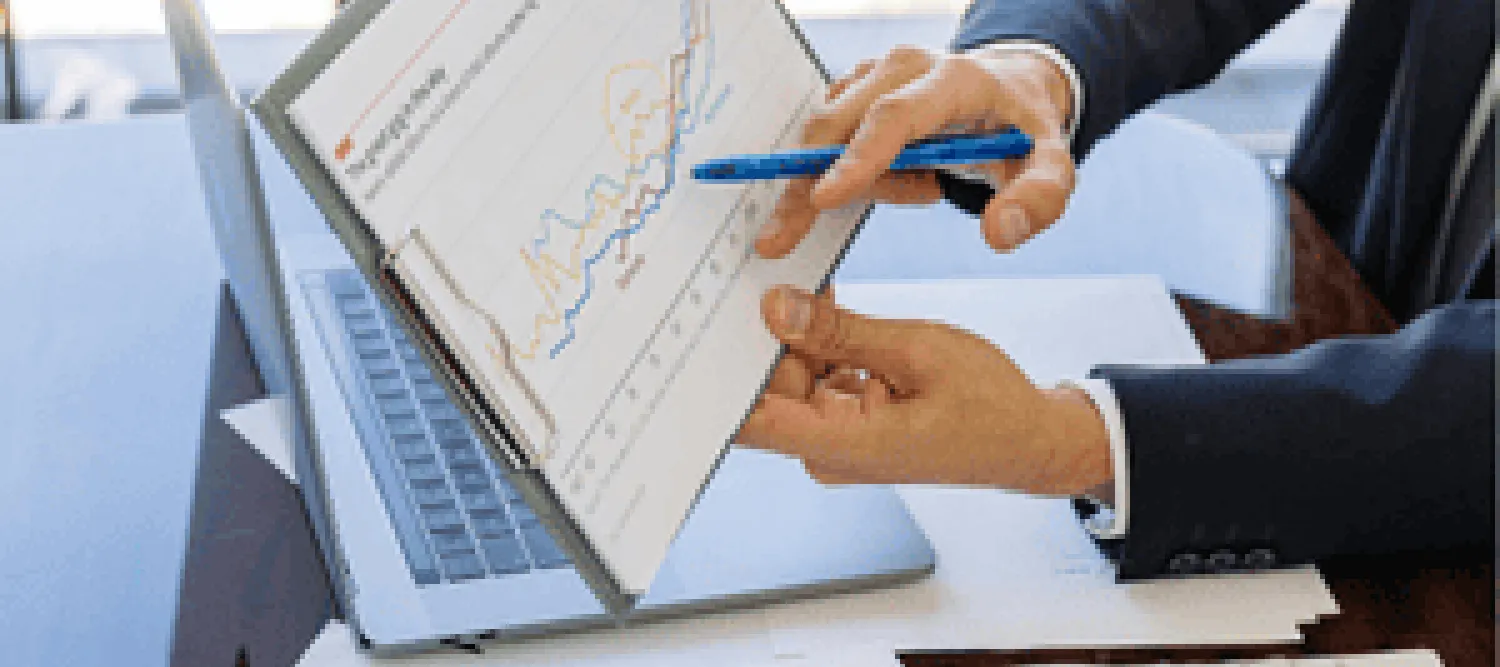 Man pointing to report with pie charts laptop in background