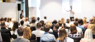 out of focus speaker in front of an audience (backs of heads in focus)