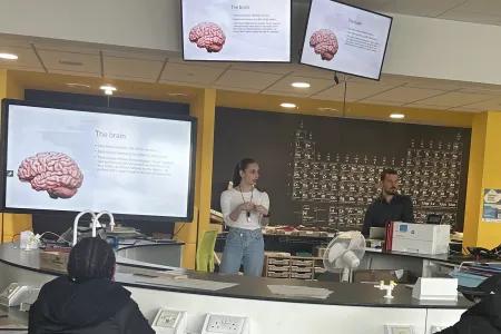 Two tutors in front of a classroom of children with visual display screens