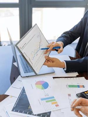 Man pointing to report with pie charts laptop in background